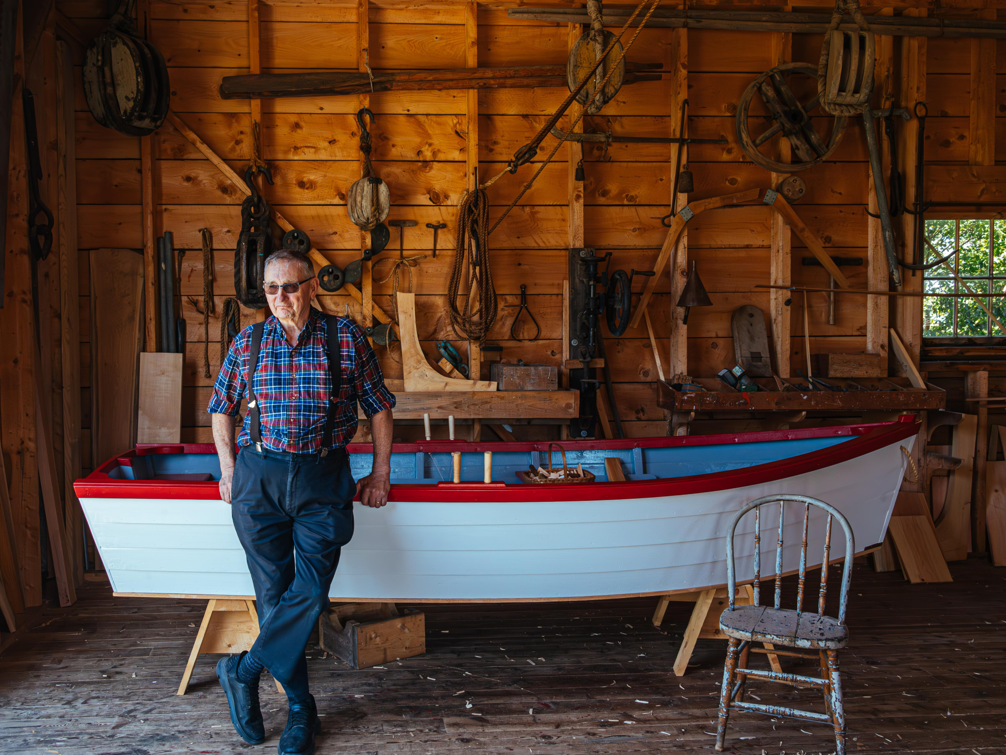 Costumed interpreter at Le Village Historique Acadien de la Nouvelle-Écosse leaning on a dory in the boat shop.